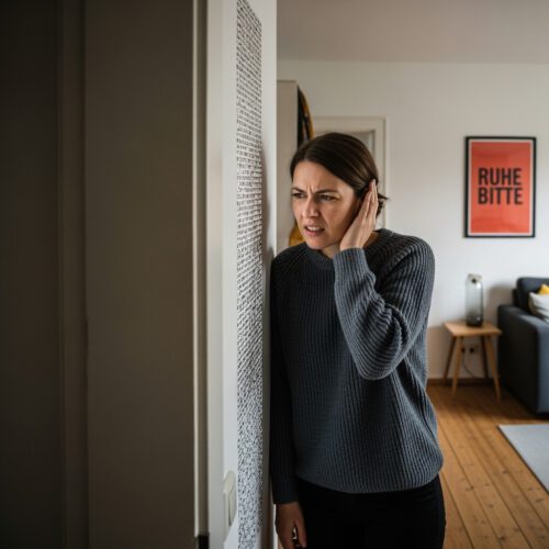 Mit besorgtem Blick lauscht eine Wohnungseigentümerin in ihrer Neubauwohnung den gravierenden Schallschutzmängeln, deren erfolgreiche Geltendmachung vor Gericht an der Verjährung scheiterte.
