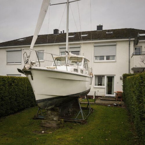 Ein großes Segelboot steht aufgebockt auf Stützen im engen, gepflegten Hinterhof eines norddeutschen Reihenendhauses.